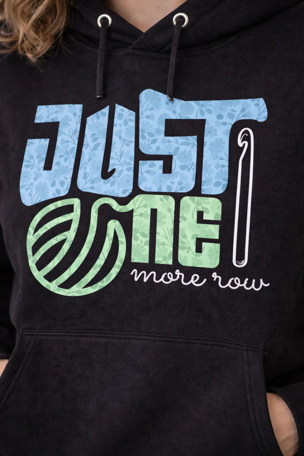 Black oversized hoodie with blue, green, and white text and graphics on a person wearing it.