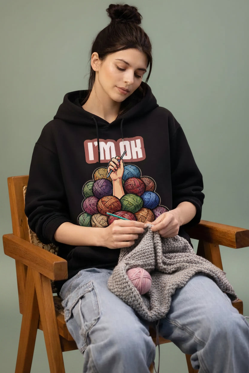 Woman knitting with a colorful yarn ball design on her oversized hoodie