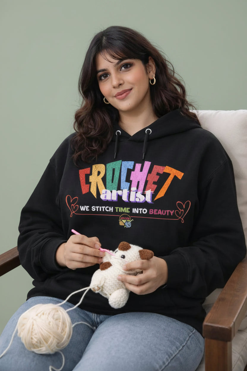 Woman wearing a black oversized hoodie with 'Crochet Artist' text, sitting outdoors with yarn and a crochet project.