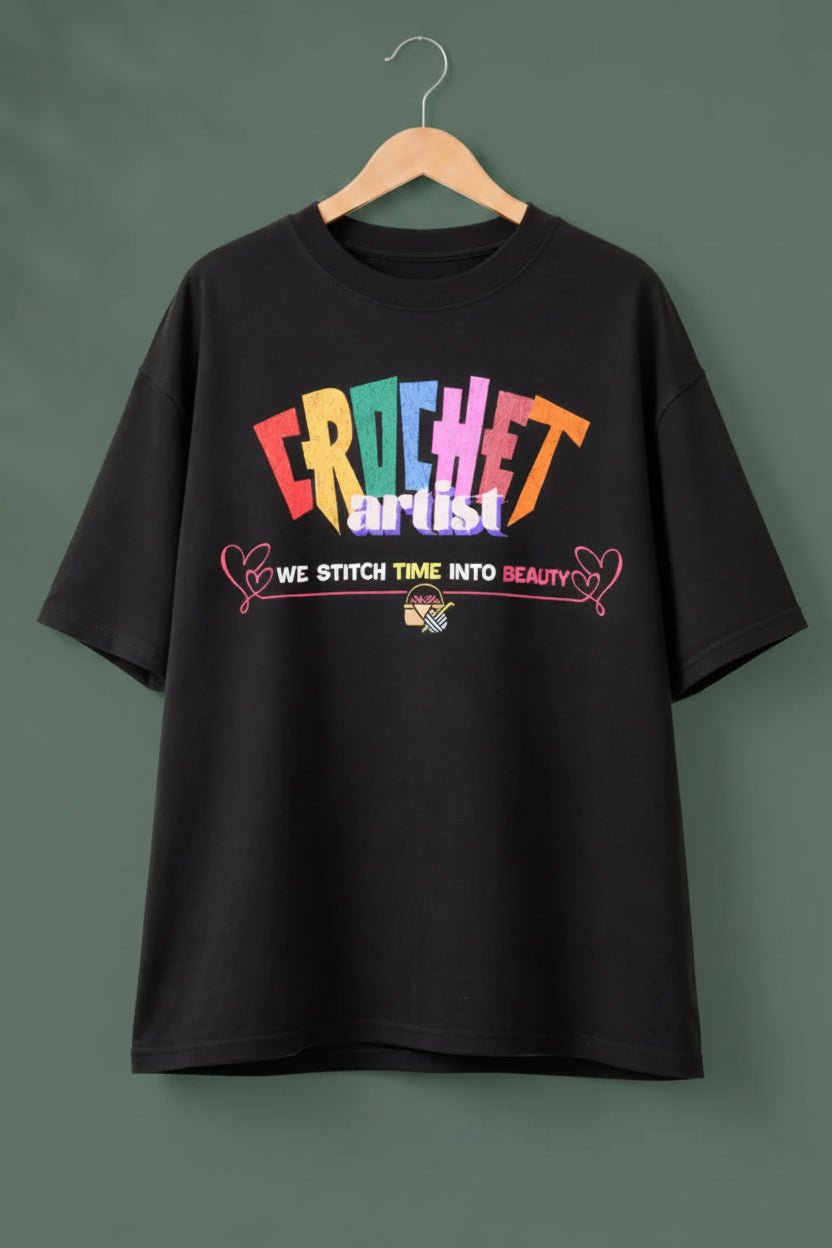 Black oversized t-shirt with text 'Crochet Artist' on a wooden hanger  