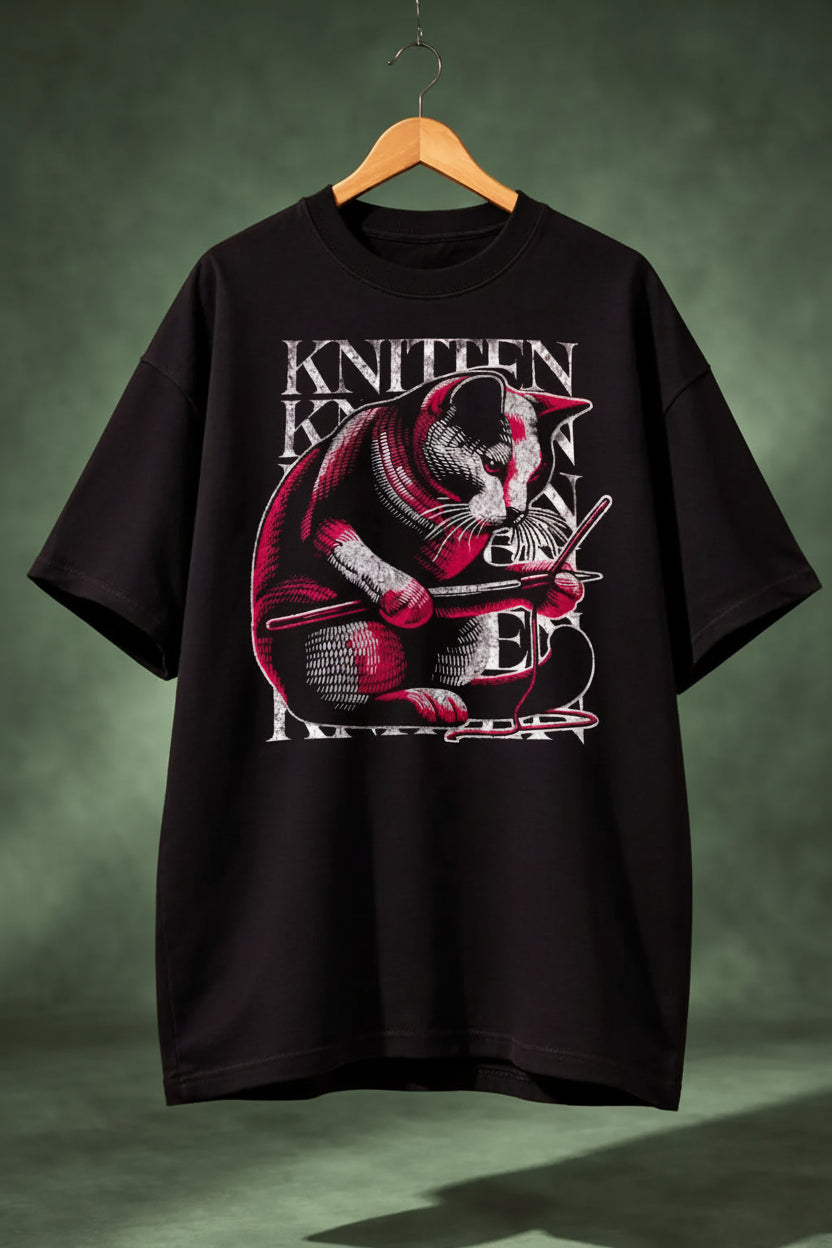 Black oversized  t-shirt with a graphic of a cat knitting and text on a wooden hanger 