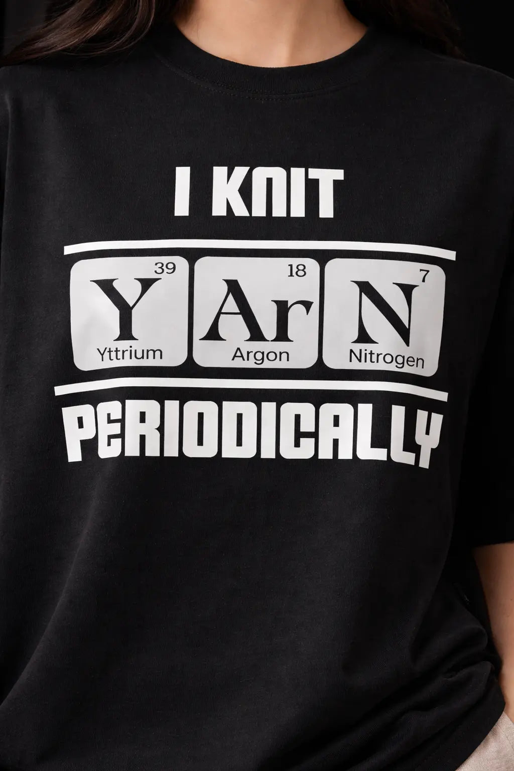 Black oversized t-shirt with white text and periodic table design, worn by a person.