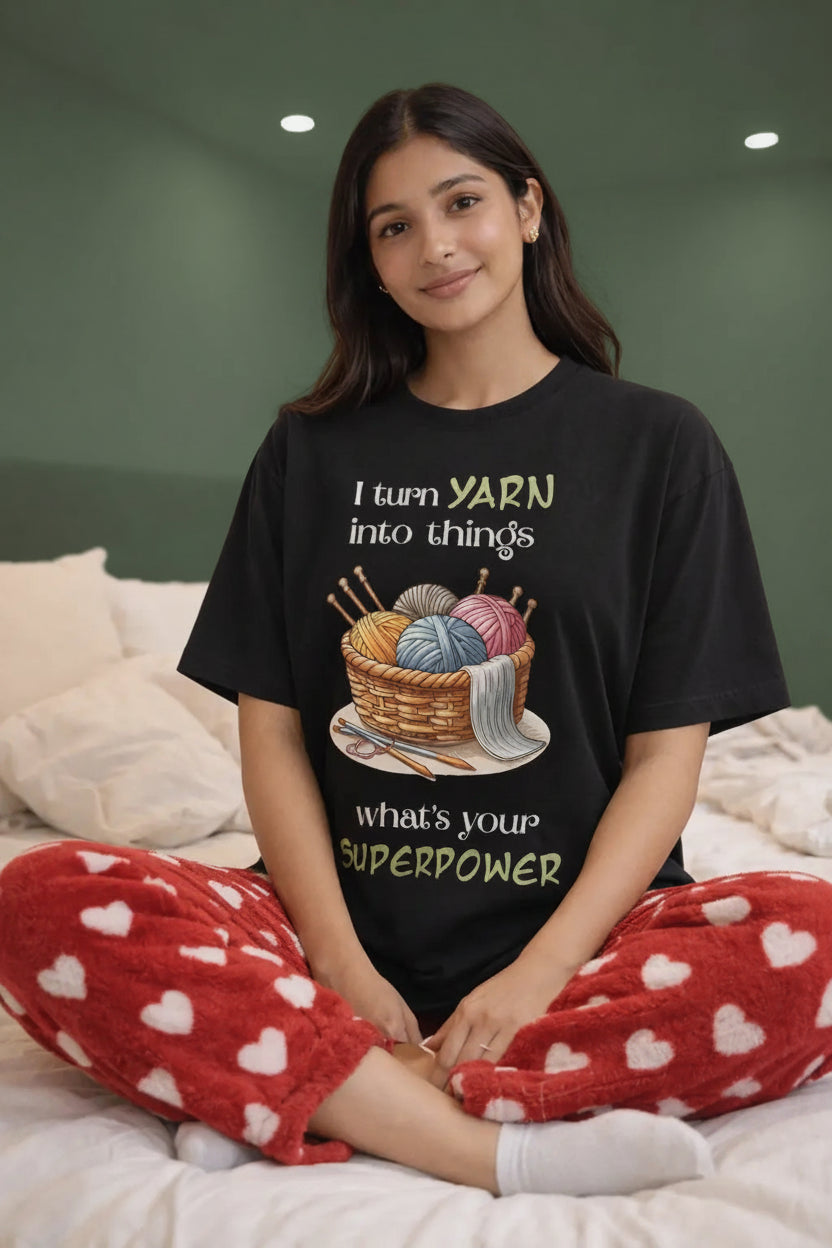 Person wearing a black t-shirt with yarn-themed design sitting on a bed.